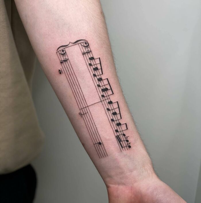 Music tattoo on forearm featuring a detailed staff and notes design.