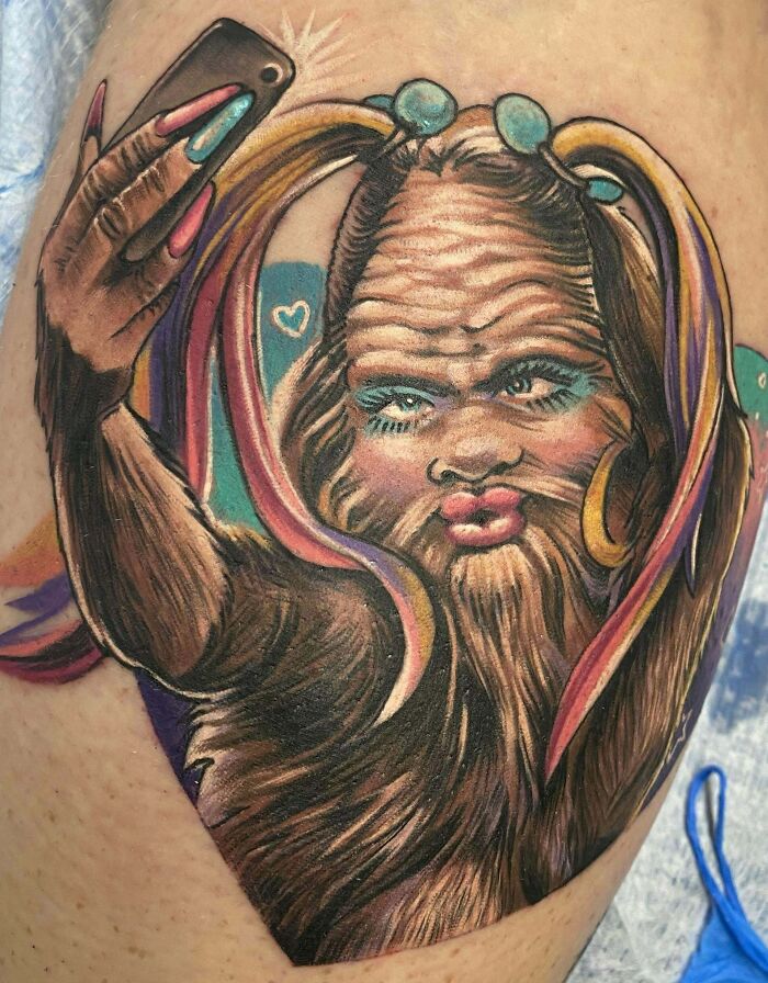 Tattoo of a hairy creature with colorful hair taking a selfie, featuring tattoos that lack foresight.