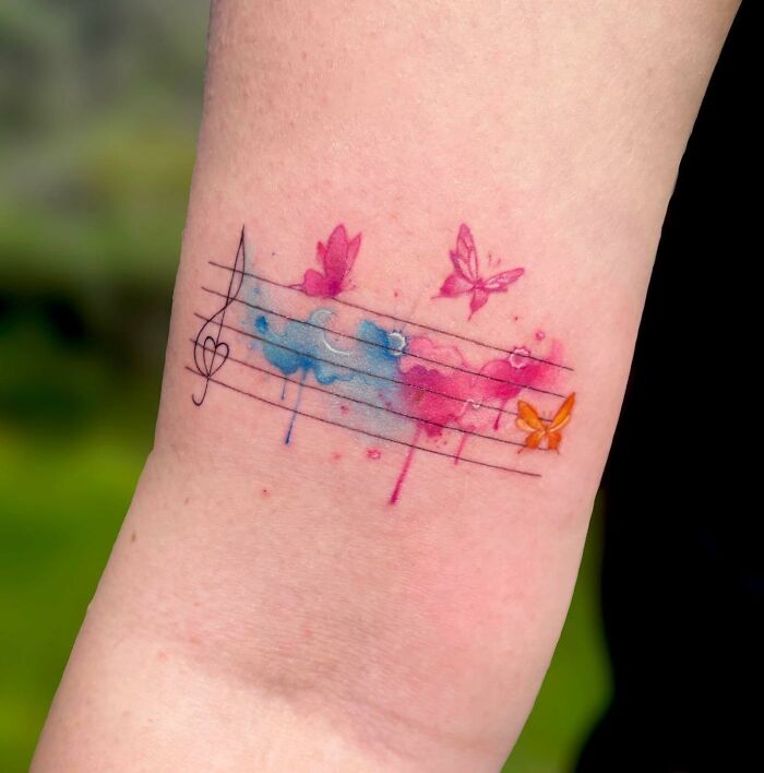 Colorful music tattoo with watercolor notes and butterflies on an arm.