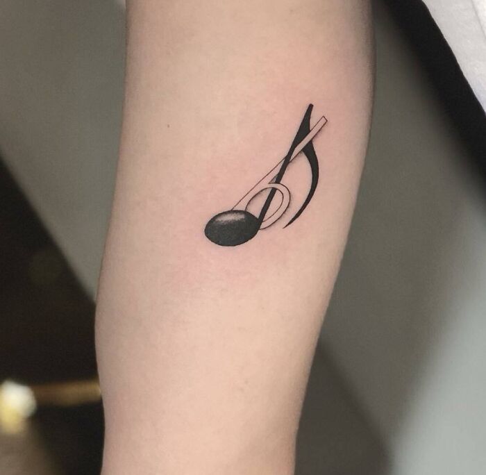 Minimalist music tattoo of a treble clef and note on forearm, capturing harmony and rhythm in ink.