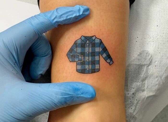 Blue checkered shirt tattoo with gloved hand on skin, example of tattoos not thought through.