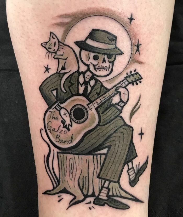 Skeleton playing guitar music tattoo, featuring a cat and a moon in the background.