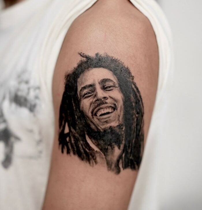 Portrait music tattoo on upper arm featuring a smiling musician icon.