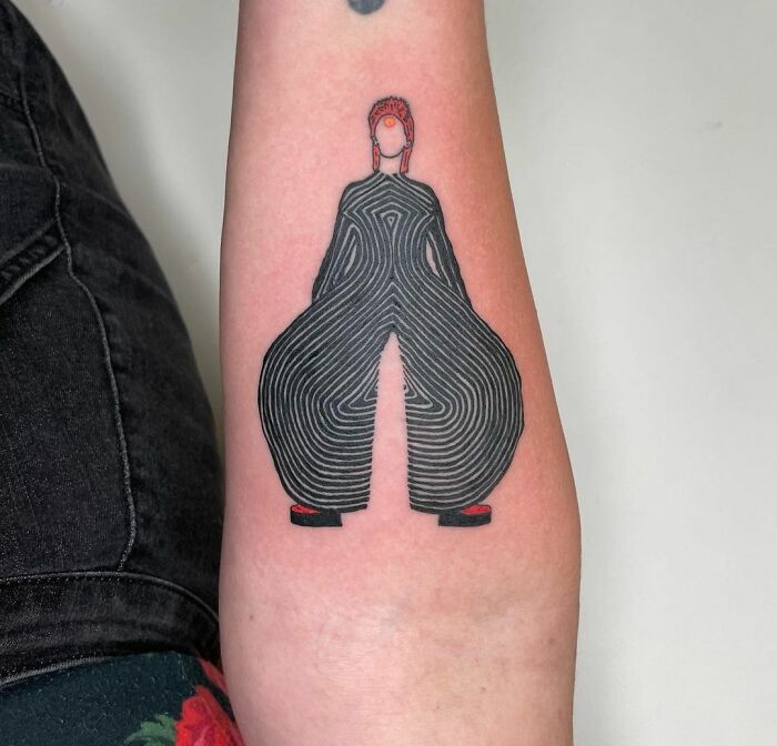 Minimalist music tattoo of a person in abstract black lines and red shoes on forearm.