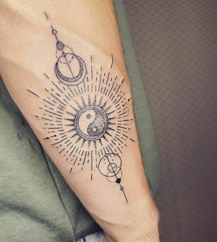 Yin Yang tattoo on forearm with intricate geometric patterns and sunburst design.