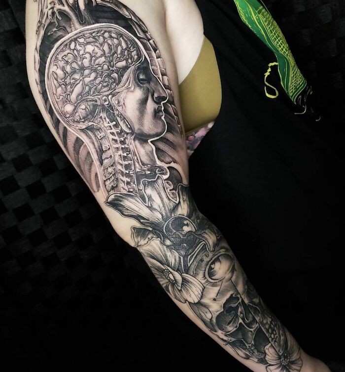 Intricate science tattoo of a human brain and skull on an arm, showcasing anatomical detail in black and gray.