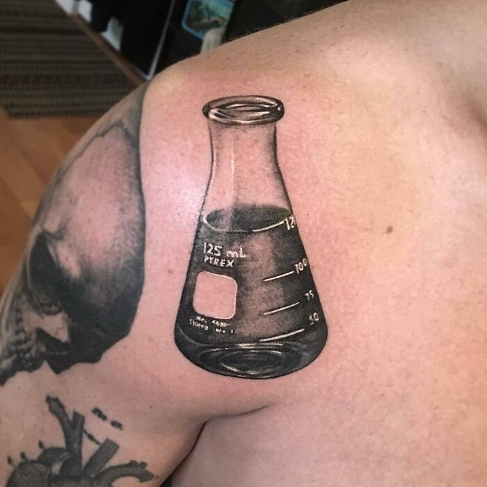 Shoulder tattoo of a beaker representing science on a person's arm.