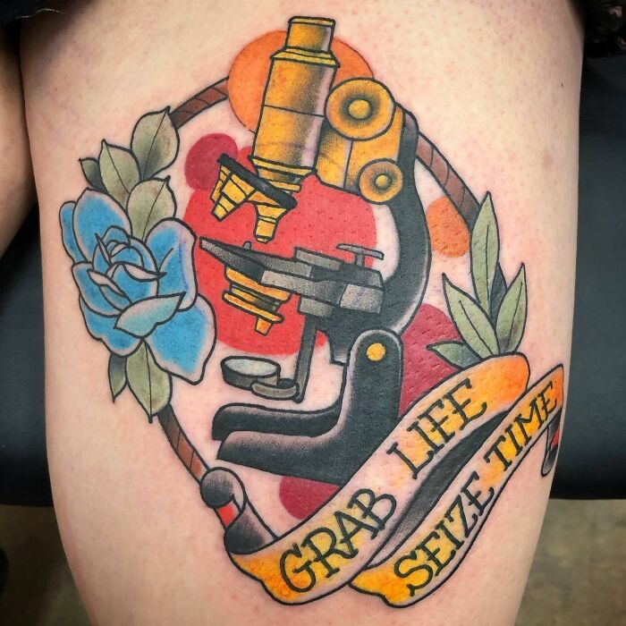 Science tattoo featuring a microscope, blue rose, and "Grab Life, Seize Time" banner in colorful ink.