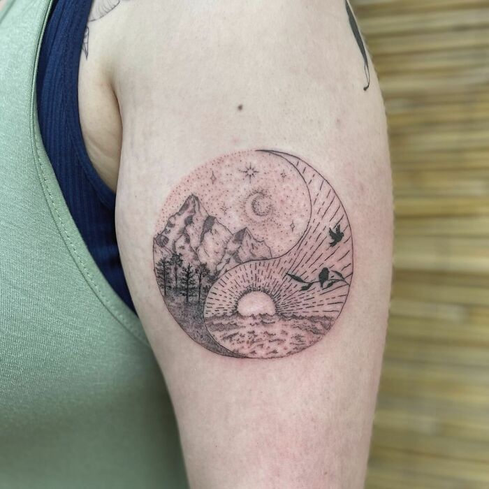Yin Yang tattoo on arm featuring nature scenes with mountains, trees, and birds, symbolizing life's duality.