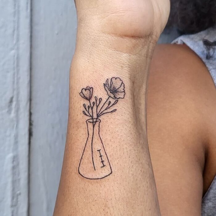 Science tattoo featuring a beaker with flowers on a forearm.