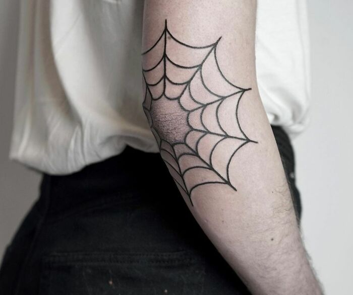 Spiderweb elbow tattoo design in black ink on an arm.