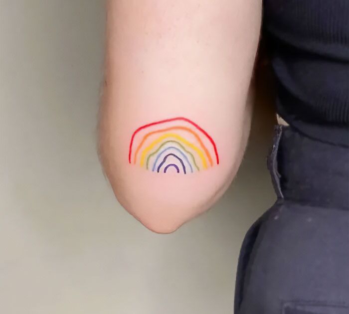 Colorful rainbow elbow tattoo design on a person's arm wearing a black shirt.