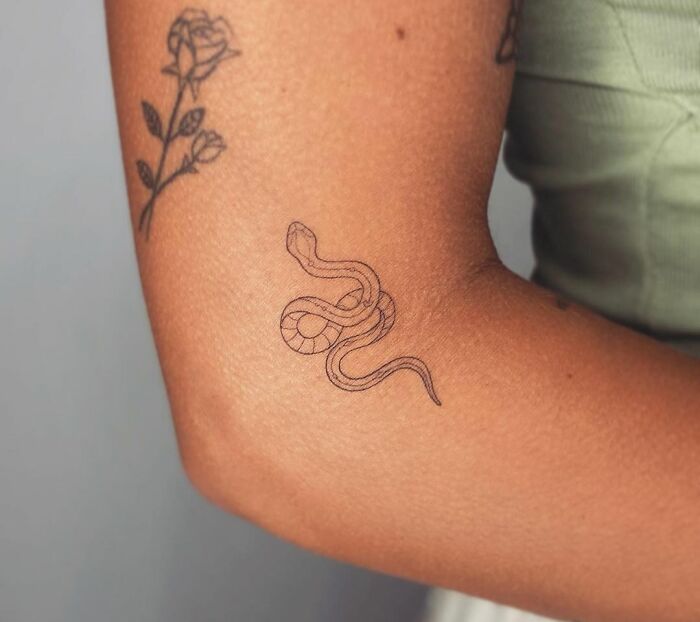Minimalistic snake tattoo on forearm alongside a floral design.