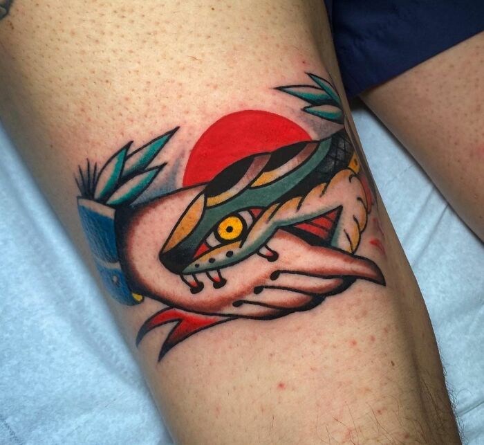 Colorful snake tattoo wrapped around a hand, featuring bold geometric shapes and a red sun background.