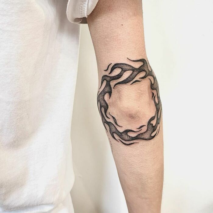 Flame-patterned elbow tattoo on an arm, blending black ink with negative space for a striking design.
