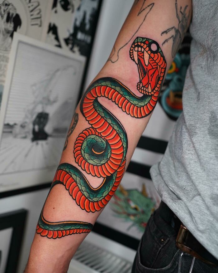 Tattoo of a vibrant, coiled snake on a person's forearm, showcasing intricate body art design.