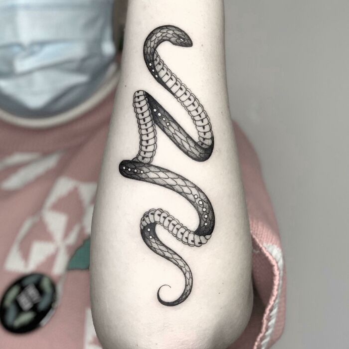 Snake tattoo design in black ink on forearm, showcasing detailed scales and curves.