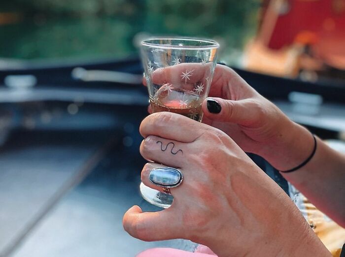 A delicate snake tattoo on a finger, with hands holding a glass.