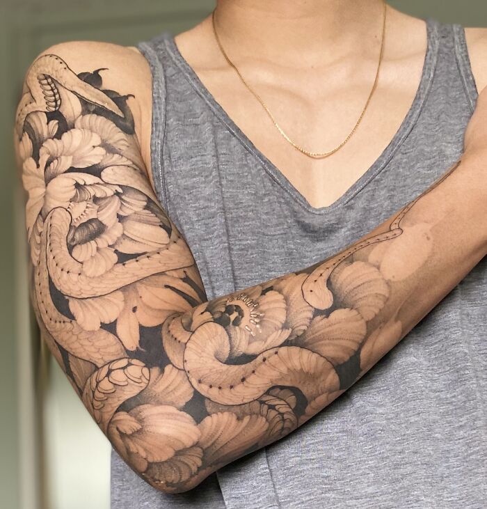 Arm with intricate snake tattoo design wrapped around, featuring bold floral elements.