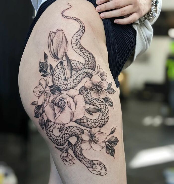 Snake tattoo on thigh featuring detailed floral designs with roses and lilies.
