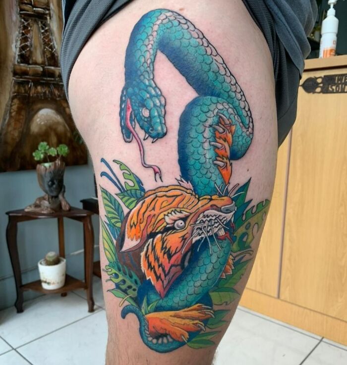 Colorful snake tattoo wrapping around a tiger on a person's thigh, showcasing intricate design and vibrant colors.