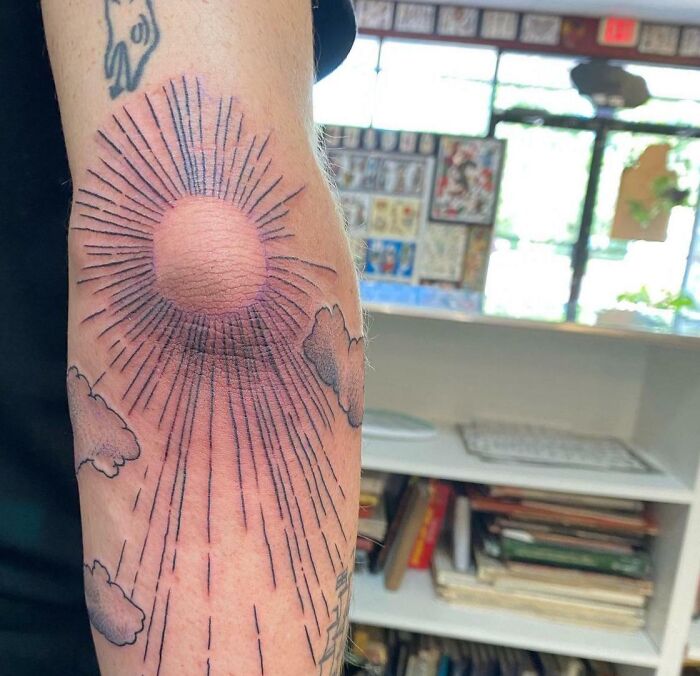 Elbow tattoo featuring a sun with rays and clouds, showcasing unique body art design.