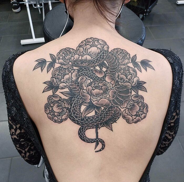Snake tattoo on a woman's back, featuring intricate floral designs.