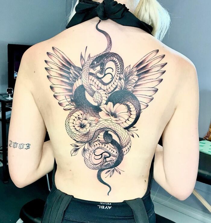 Intricate snake tattoo on a woman's back, featuring wings and flowers.