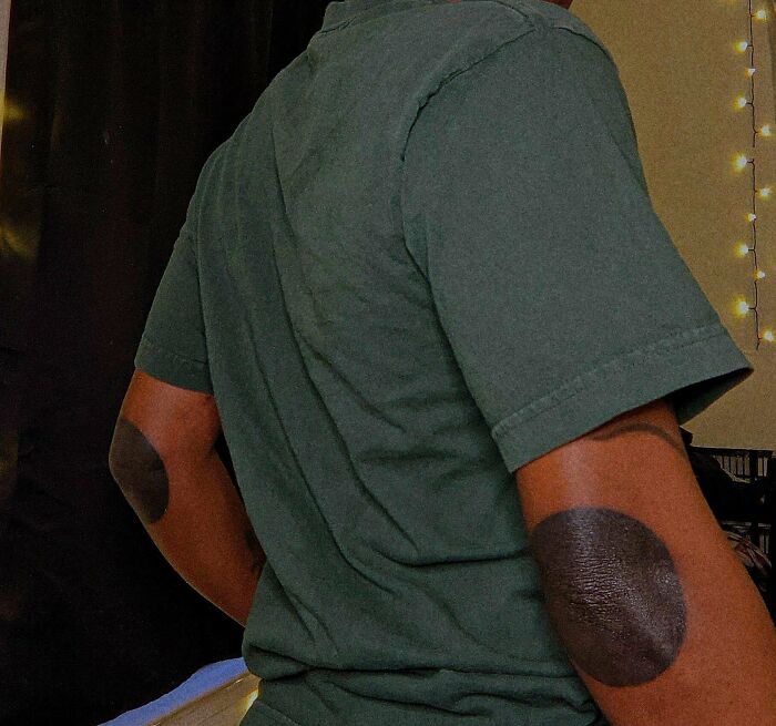 Person in a green shirt showcasing solid black elbow tattoos indoors.