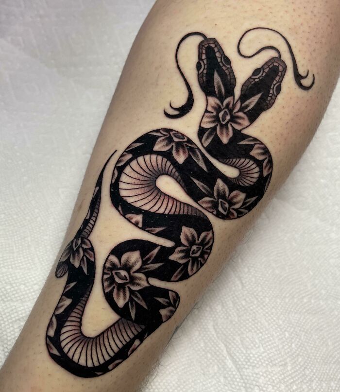 Snake tattoo with floral designs on a forearm, showcasing intricate details and bold contrast.