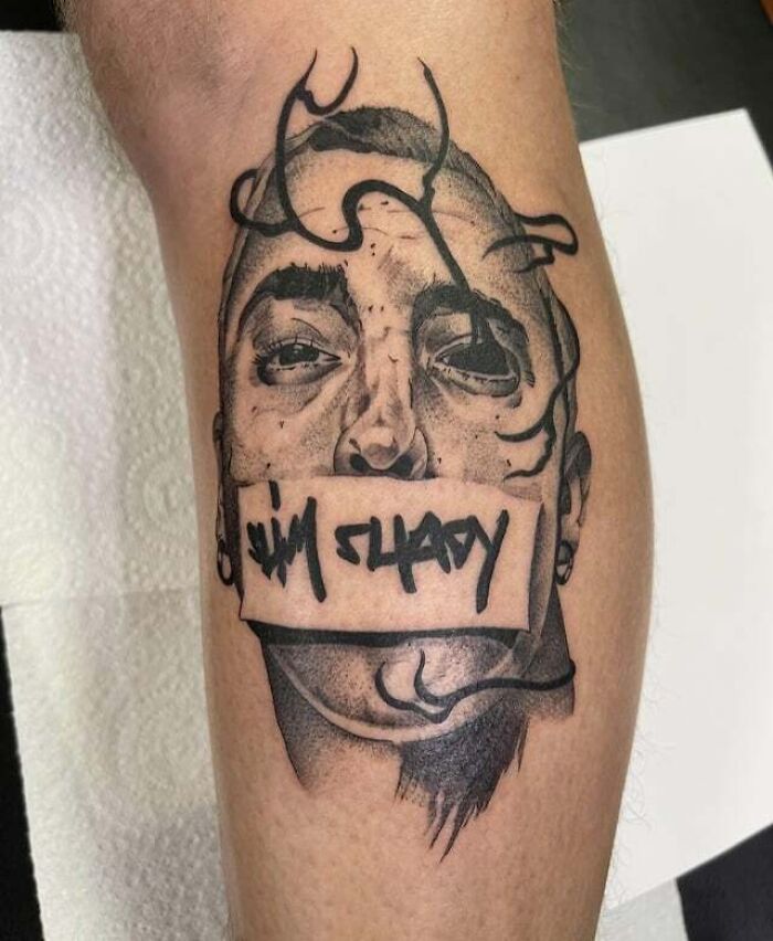 Tattoo of a '90s cultural figure with the words "Slim Shady" across the mouth on someone's leg.