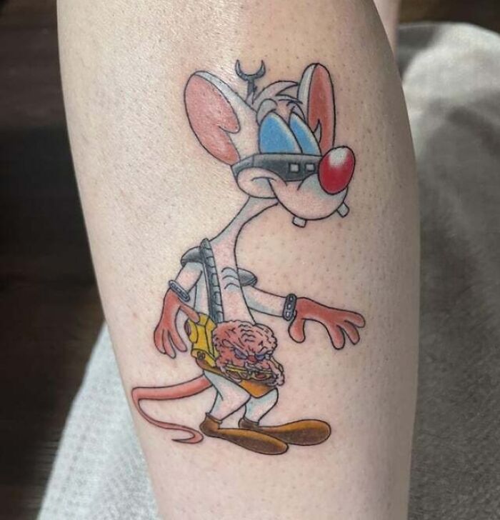 Cartoon mouse tattoo from the '90s, on a person's leg, featuring a brain character in a pouch.