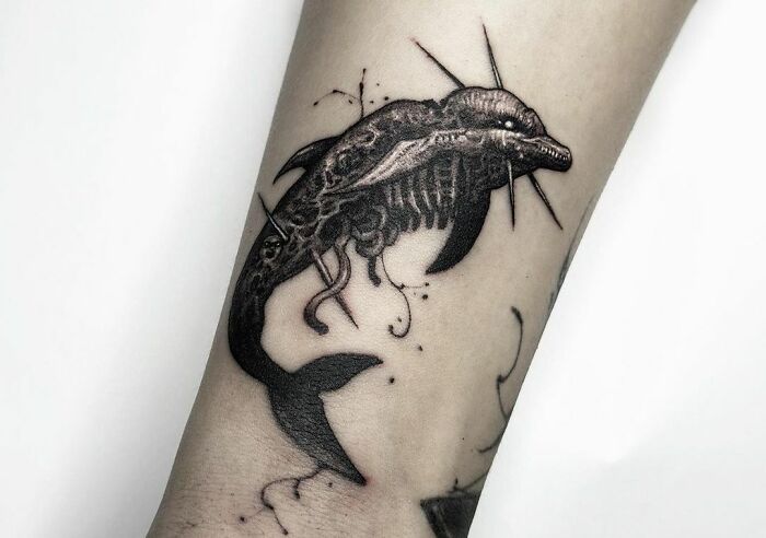 Forearm with an intricate gothic tattoo of a dolphin skeleton design.