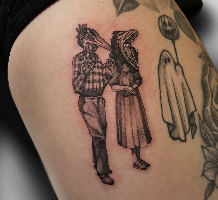 Gothic tattoo of a couple with bird heads on an arm, featuring spooky details and unique linework.