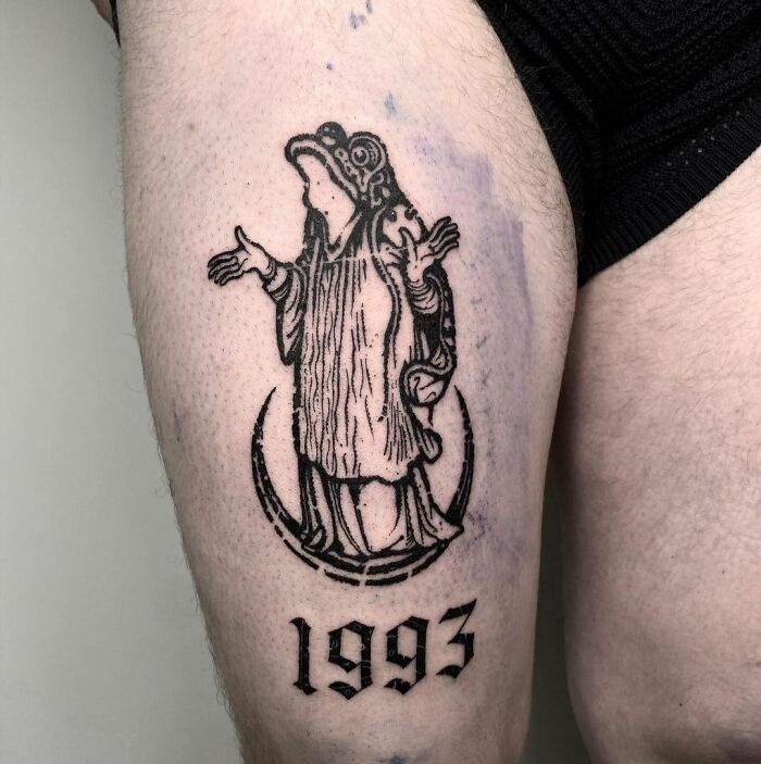 Gothic tattoo of a robed figure and the year 1993 inked on a person's thigh.