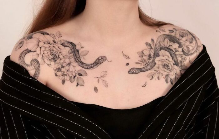 Snake tattoos with floral design on woman's shoulders, featuring detailed snake wrapping among flowers.
