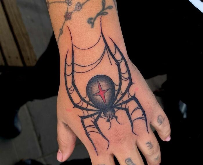 Hand with a gothic tattoo of a spider with web details, showcasing intricate design elements.