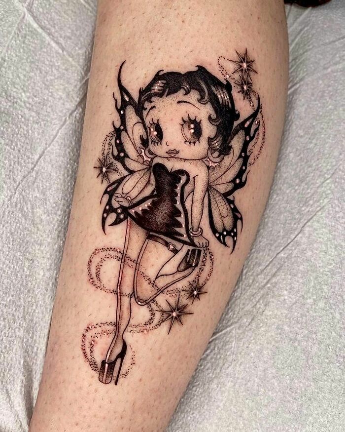 ‘90s tattoo of a fairy character in a black dress with wings, featuring star and swirl details on skin.