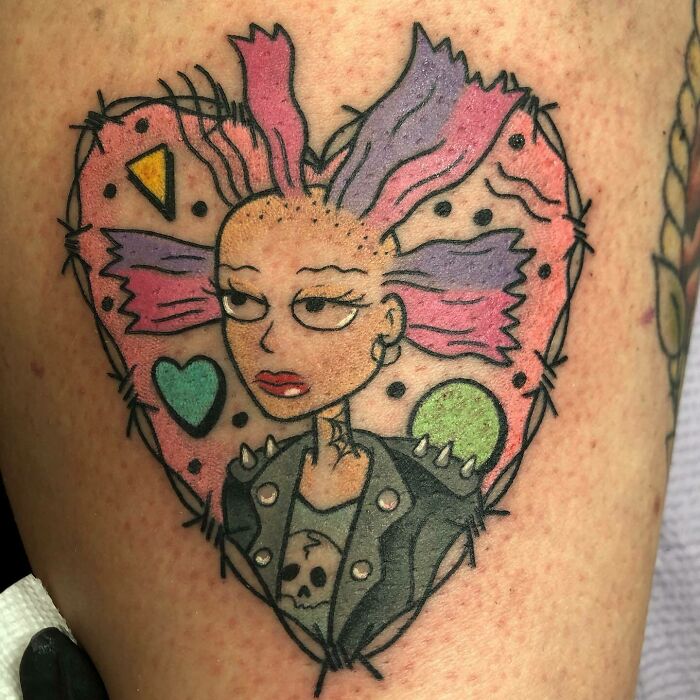 '90s tattoo featuring a cartoon punk character with colorful hair, surrounded by geometric shapes and a pink heart.