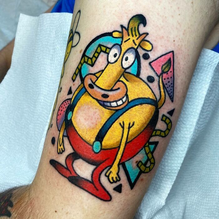 Colorful '90s cartoon character tattoo of a yellow bull with blue suspenders and red pants on an arm.