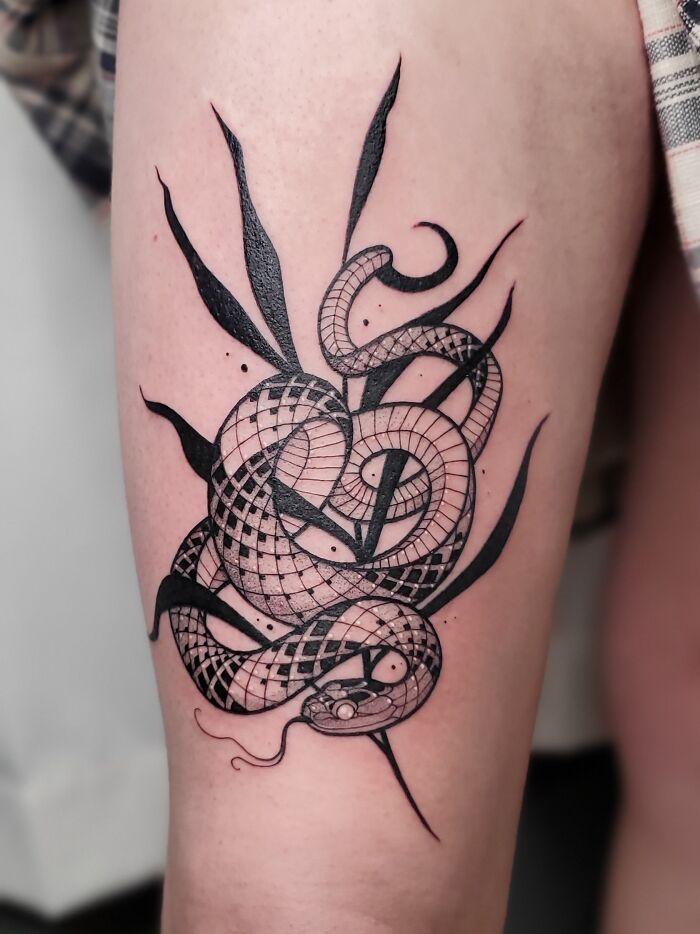 Black and white snake tattoo intricately wrapped around a forearm, showcasing detailed patterns and design elements.