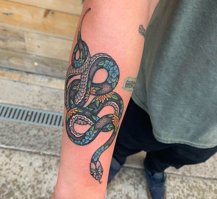 Colorful snake tattoo with floral details on a person's forearm.