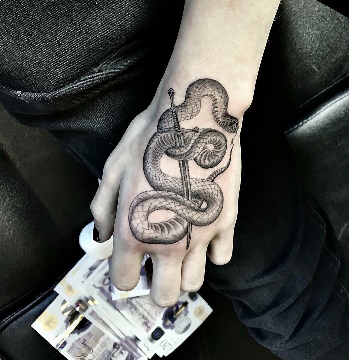 Snake tattoo on a hand, featuring a detailed design of a snake wrapped around a dagger.