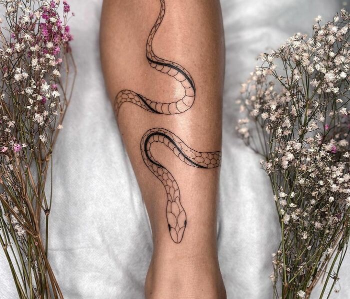 Snake tattoo design on a person's leg, surrounded by delicate flowers.