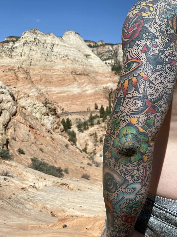 Colorful elbow tattoo with eye and rose designs against a desert landscape background.