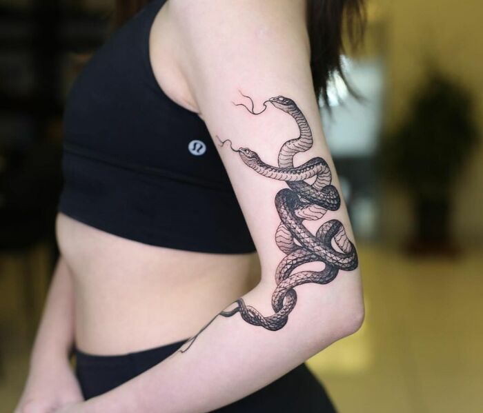 Snake design on elbow tattoo, featuring intricate black linework on a woman's arm, showcasing dazzling tattoo artistry.