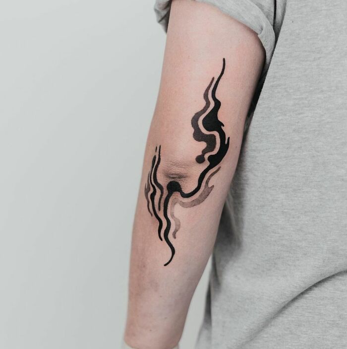 Abstract black ink design as an elbow tattoo on a person's arm.