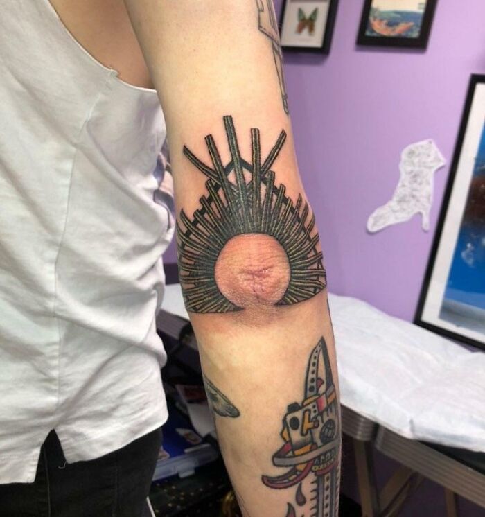 Elbow tattoo featuring a sunburst design on a person's arm, displayed in a tattoo studio.