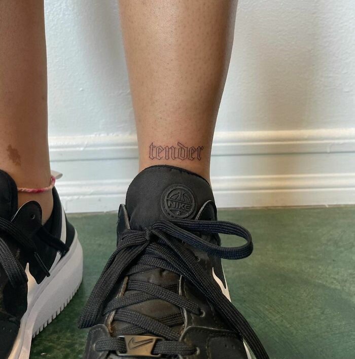 Ankle tattoo reading "tender" above a Nike sneaker.