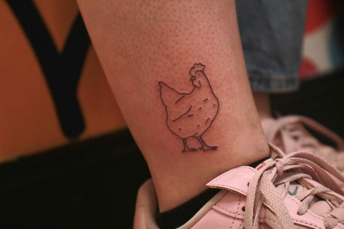 Ankle tattoo of a chicken near a pair of pink sneakers.